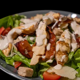 Insalata Caesar con pollo grigliato a fette, bacon croccante, lattuga, pomodori, crostini e salsa cremosa